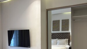 Quarto de hotel moderno com cama, televisão de tela plana, guarda-roupa e espelho refletindo o ambiente.