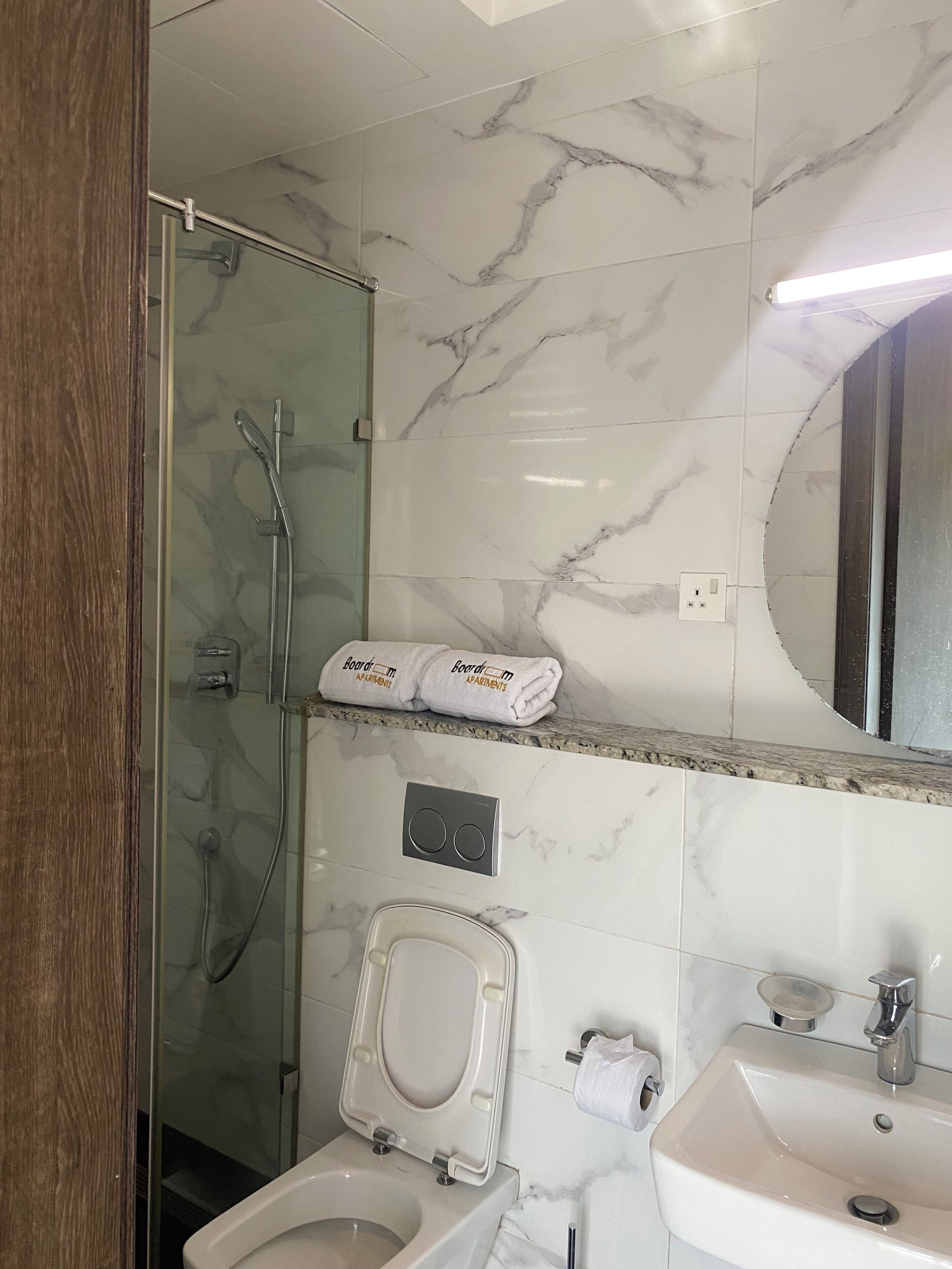 Une salle de bain avec une douche à parois de verre, des toilettes, un lavabo et un porte-serviettes avec des serviettes pliées.