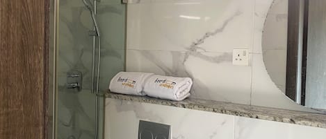 Une salle de bain avec une douche à parois de verre, des toilettes, un lavabo et un porte-serviettes avec des serviettes pliées.