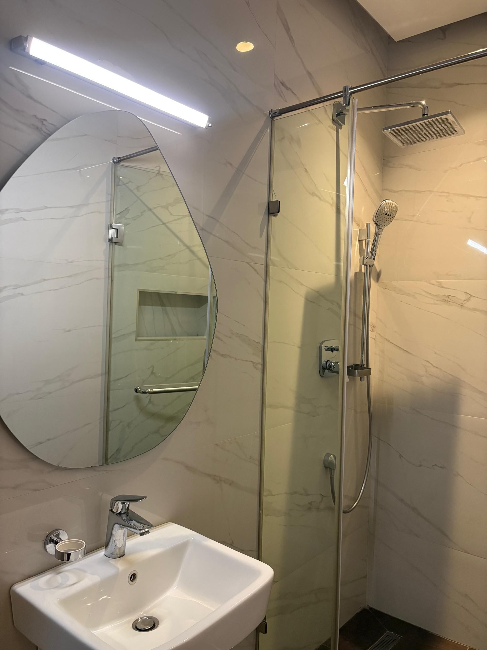 A modern bathroom with a glass-enclosed shower, a white sink, and a large mirror.
