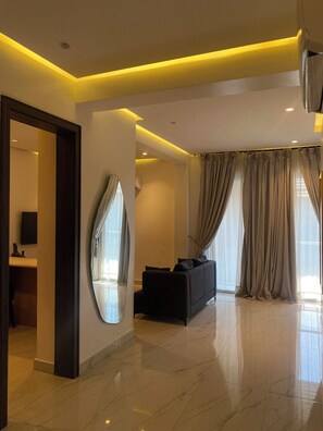 A modern living room with a large mirror, a black sofa, and a television. - Boardroom Apartment  by Jotani Living  (Lekki)