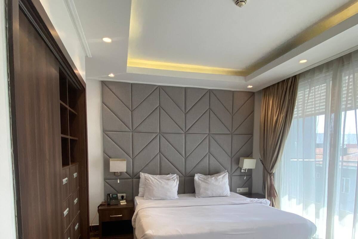 Een moderne hotelkamer met een groot bed, een kledingkast, een nachtkastje en uitzicht op de stad.