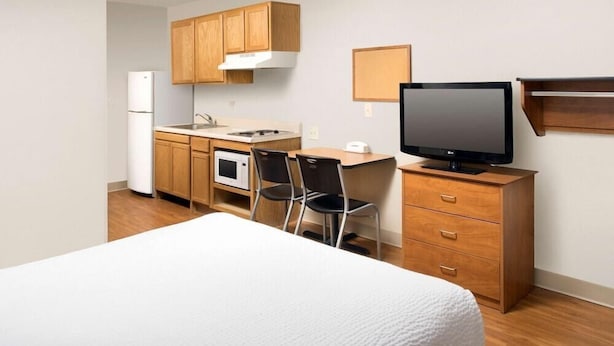 A compact hotel room with a kitchenette, a bed, a TV, and a desk.