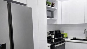 Una cocina moderna con armarios blancos, un refrigerador de acero inoxidable, un horno negro y un microondas en un estante.
