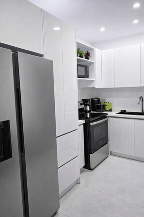 Eine moderne Küche mit weißen Schränken, einem Edelstahl-Kühlschrank, einem schwarzen Backofen und einer Mikrowelle auf einer Ablagefläche.