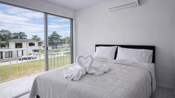 Habitación de hotel moderna con una cama grande, un balcón con vistas a la calle y edificios, y un equipo de aire acondicionado en la pared.