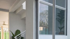 Un interior moderno con una escalera que lleva a un balcón, una planta grande en maceta y vistas al exterior.