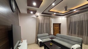 A living room with a sectional sofa, a flat-screen TV, a coffee table, and a ceiling fan. - Sadachandra Home Stay (Kundapur)