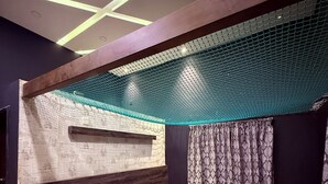A modern bedroom with a bed, a headboard, a bedside table, a lamp, and a patterned curtain. - Sadachandra Home Stay (Kundapur)