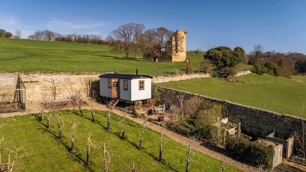 A small, single-story house with a stone wall and a garden. - Plank Bridge | Shepherds Hut in Apple Orchard | Sleeps 2 (West Ayton)