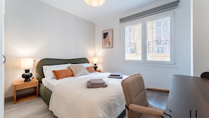 Une chambre à coucher avec un lit, des lampes de chevet, une chaise, un bureau et une fen être donnant sur un beau paysage.