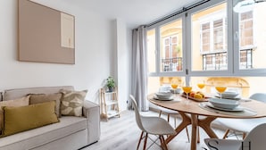 Un salon moderne comprenant un canapé, une table à manger avec des chaises et de grandes fenêtres donnant sur la rue.
