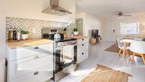 A modern kitchen with a built-in oven, a stainless steel range hood, and a wooden countertop. There is a dining area with a white table and chairs, and a TV on a wooden stand. - Steps 2 Sand | Magical Sunsets | Carefree Checkout (Indian Rocks Beach)