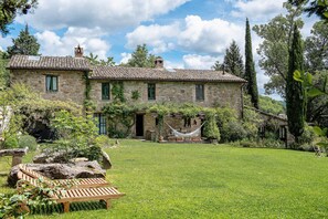 Una casa de pedra amb teulada de rajola, un hamaca i un pati amb gespa.