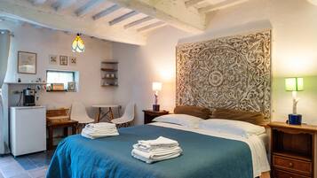 A bedroom with a bed, bedside tables, a desk, chairs, a coffee machine, and a decorative headboard.