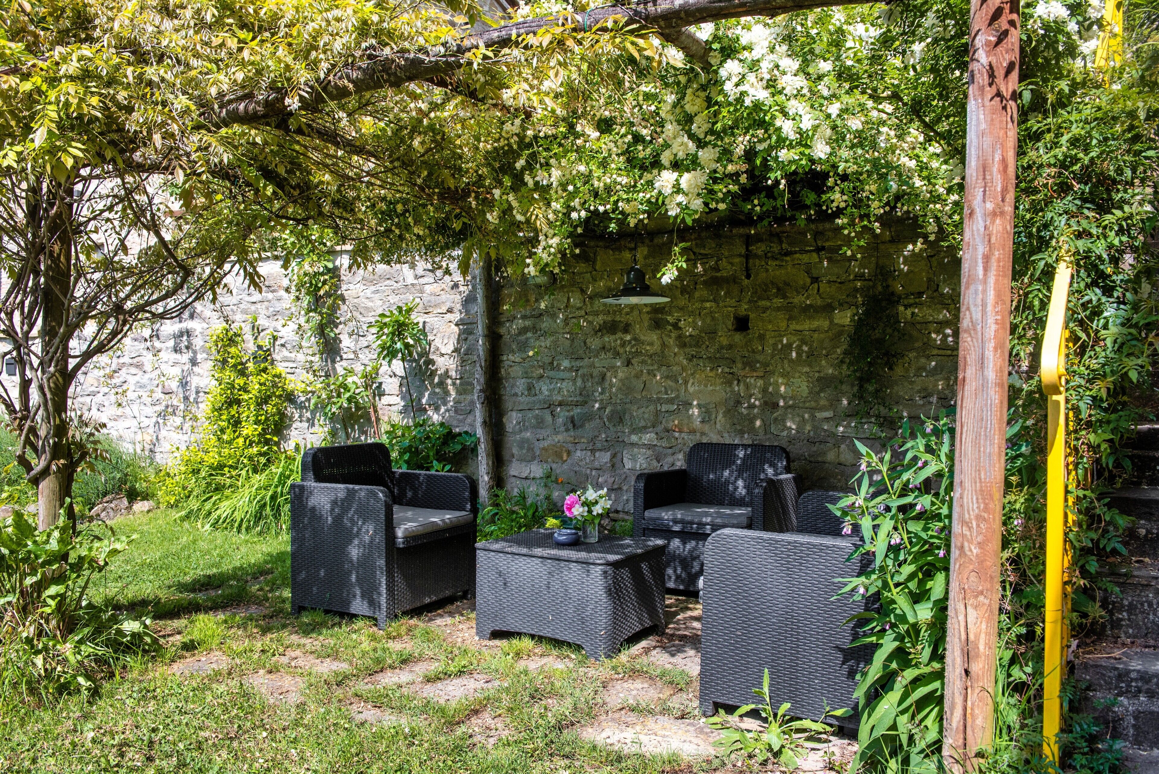 Un patio con mobiliario de mimbre, un muro de piedra y vegetación.