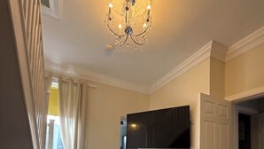 Amplia sala de estar con candelabro, televisor de pantalla plana en la pared y radiador.