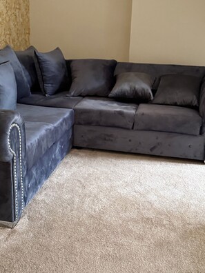A sectional sofa with a dark fabric and decorative stitching, positioned on a beige carpet in a room with a plain wall and a textured wallpaper on one side. - modern luxury cottage (Ayr)