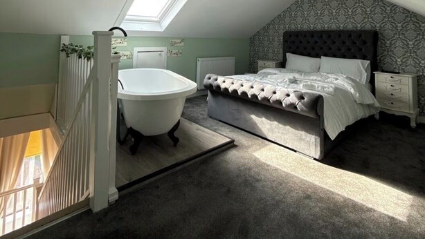 Un dormitorio con una cama grande, una bañera blanca y un tragaluz.