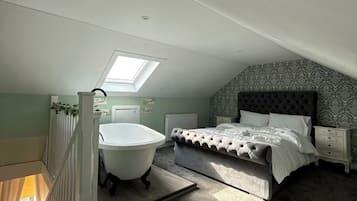 A bedroom with a large bed, a white bathtub, and a skylight.