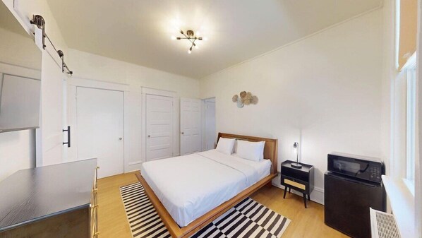 A bedroom with a bed, bedside tables, a desk, a microwave, and a ceiling light fixture. - Ocean Breeze Hotel (Ocean City)