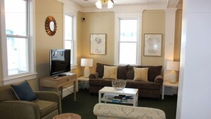 Una sala de estar con sofá, sillón, reposapiés, televisión y dos mesitas de noche con lámparas.