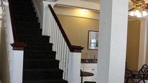 Una escalera con alfombra oscura y columnas blancas que conduce a un comedor con mesas y sillas.