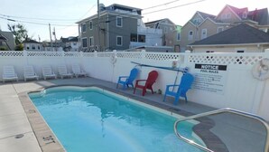 Una piscina con cerramiento blanco, sillas de descanso y un tablón de anuncios.