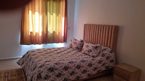 A bedroom with a bed, a nightstand, and a window with curtains. - Luxurious Accessible Apartment in the Heart of Fes (Fes)