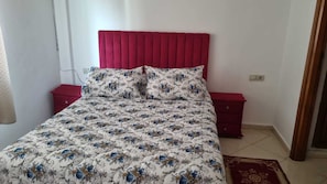 A bed with a floral bedspread, a red upholstered headboard, and two nightstands with red drawers. - Luxurious Accessible Apartment in the Heart of Fes (Fes)
