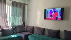 Una sala de estar con un sofá verde, un televisor montado en la pared y una ventana con cortinas.
