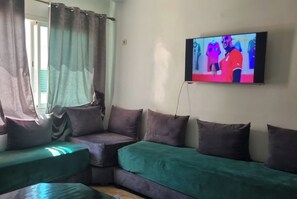 A living room with a green sofa, a TV mounted on the wall, and a window with curtains. - Luxurious Accessible Apartment in the Heart of Fes (Fes)