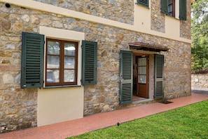 Ein Steinhaus mit zwei Fenstern und einer Tür, alle mit grünen Fensterläden.