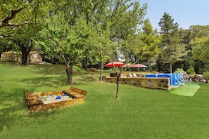 Ein Garten mit Sandkasten, einem kleinen Baum und einer blauen Spielzone.