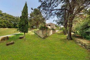 Une maison en pierre avec un mur en pierre, entourée d’une pelouse bien entretenue et d’arbres.