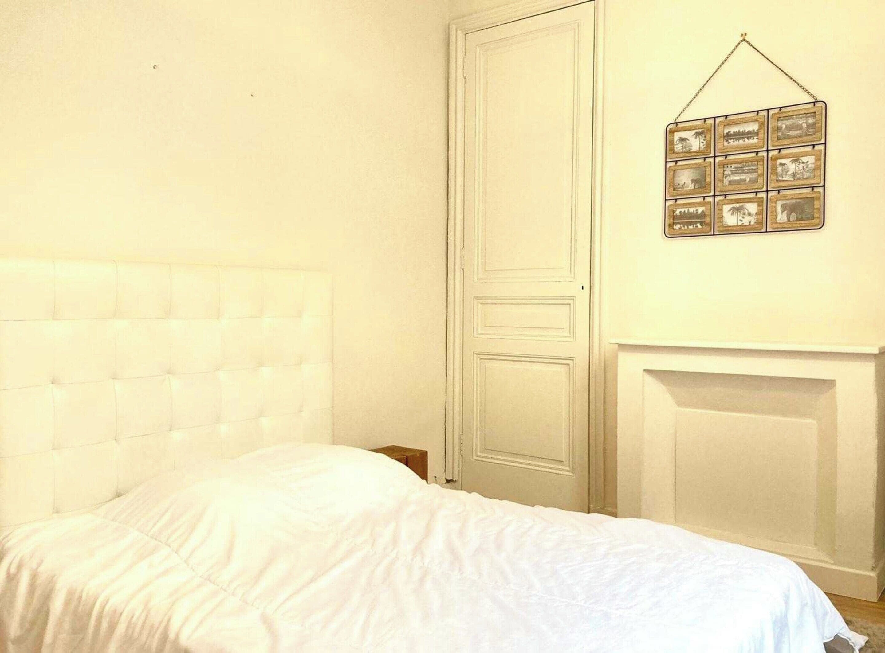 A bedroom with a tufted headboard, a white bedspread, a white door, and a wall-mounted picture frame.