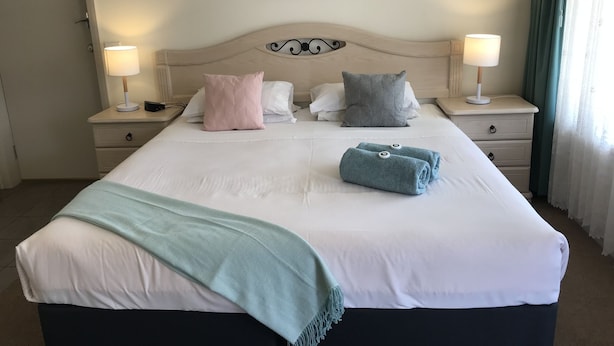 A neatly made bed with pillows, a blanket, and towels. There are two bedside tables with lamps. A painting hangs on the wall above the bed. - City Central Motor Inn And Apartments (Warrnambool)