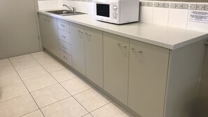 A kitchen with a microwave, sink, and light-colored cabinets. - City Central Motor Inn And Apartments (Warrnambool)