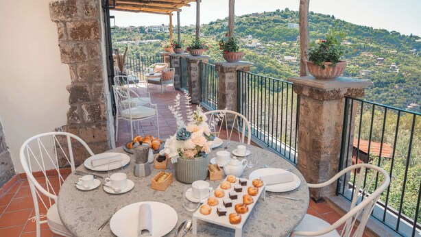 A terrace with round tables set for dining, surrounded by potted plants and a scenic view of a hilly landscape. - Borgo Mezzo Monte. Panoramic Sea View,Jacuzzi and Concierge by Feeling Italy (Sorrento)