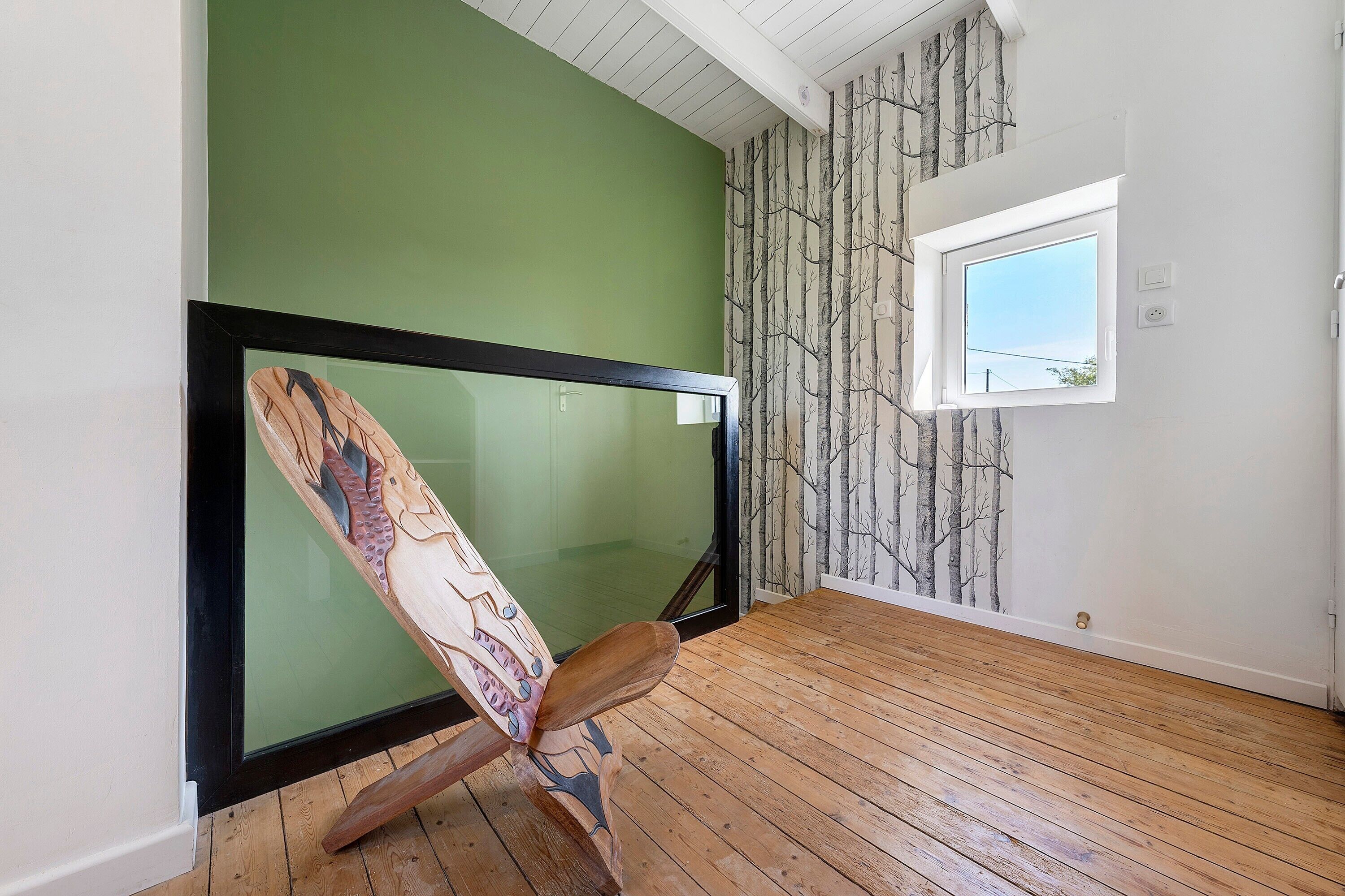 A room with a green wall, a wooden floor, a framed artwork, a window, and a wall with a tree pattern.