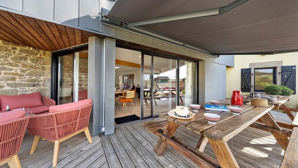 An outdoor patio with wicker furniture, a wooden table, and a glass door leading to an interior space. - Kerlonie Family Haven: Spacious Holiday Home with Private Terrace, Wi-Fi & Air Conditioning (Kerlouan)
