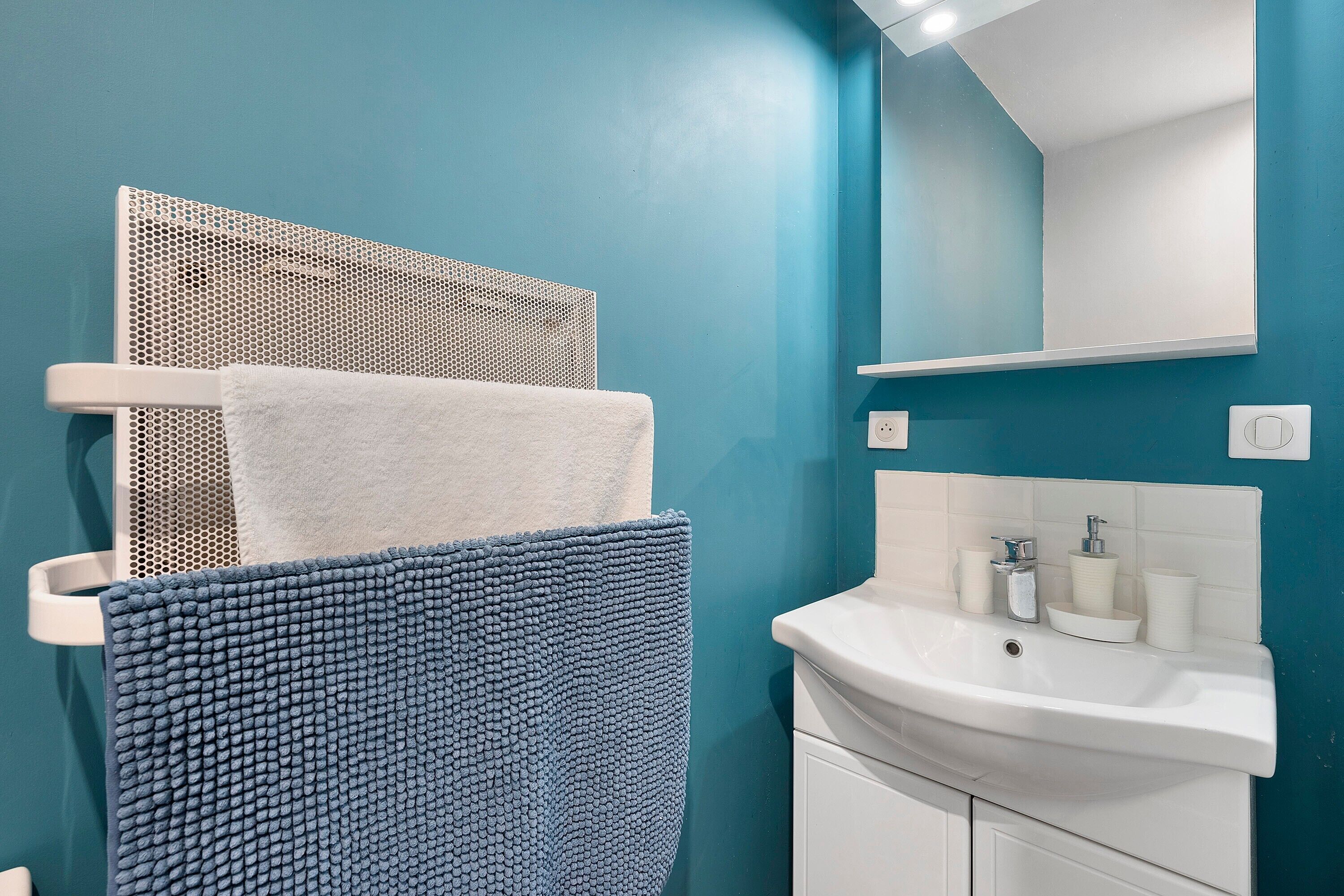 Une salle de bain avec un lavabo blanc, un miroir et un porte-serviettes sur lequel est posée une serviette blanche.