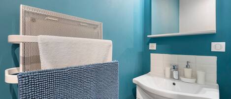 Une salle de bain avec un lavabo blanc, un miroir et un porte-serviettes sur lequel est posée une serviette blanche.