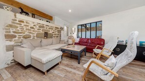 A living room with a stone wall, a sofa, a red leather couch, a wooden coffee table, and a wicker chair. - Kerlonie Family Haven: Spacious Holiday Home with Private Terrace, Wi-Fi & Air Conditioning (Kerlouan)