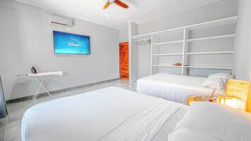 Una habitación de hotel moderna con dos camas, un televisor que muestra el logo de Disney+ y un ventilador de techo, además de un armario con estantes.