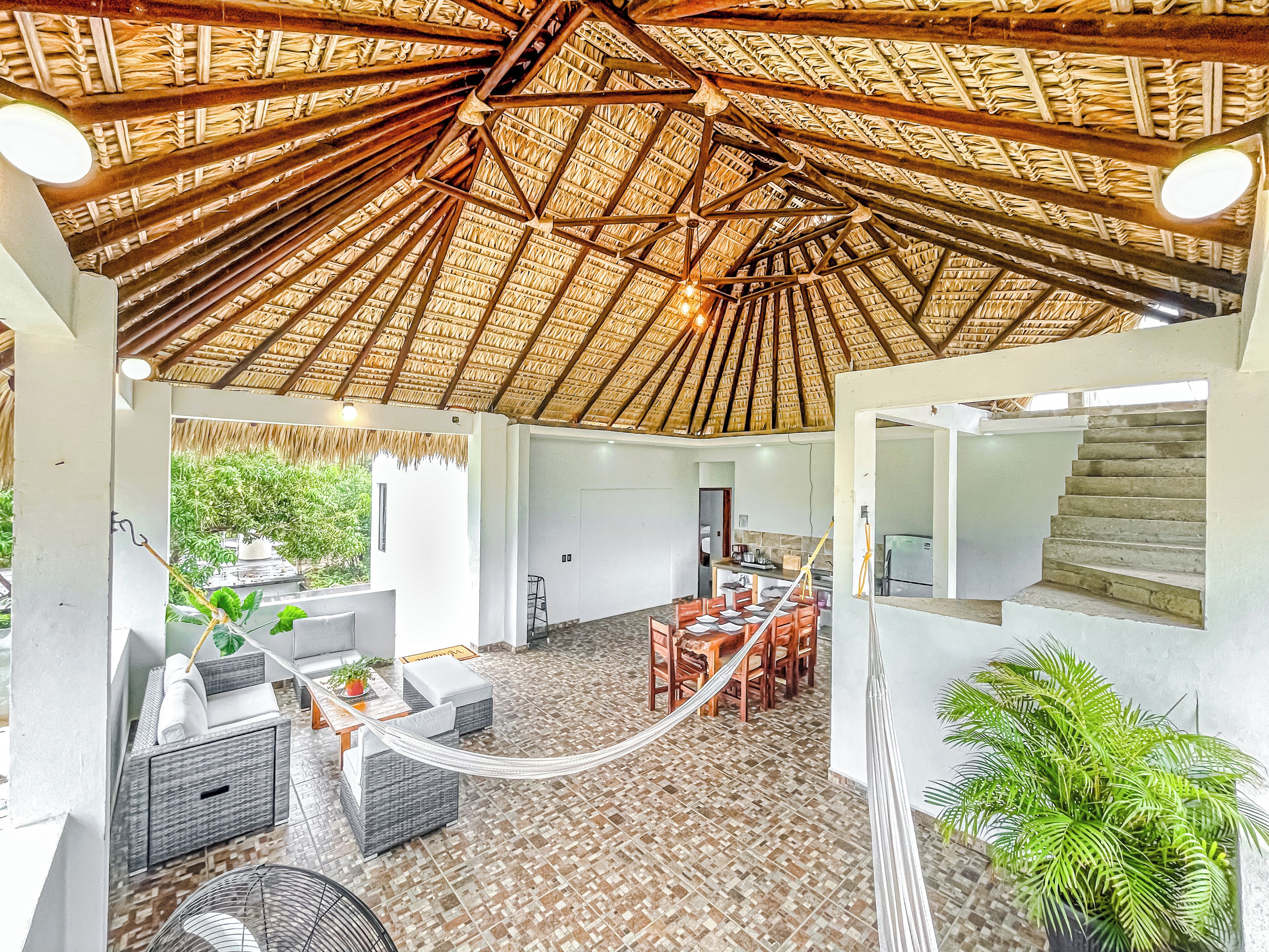 Un espacio interior amplio con techo alto, zona de comedor con mesas y sillas, y una escalera.