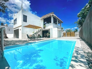 Una casa moderna con piscina, arredi da esterno e una struttura con tetto di paglia.