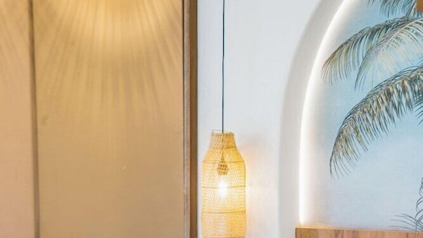 A hotel room with a bed, a wall-mounted painting, a table with wine bottles and glasses, and a hanging light fixture. - Drossia Hotel (Hersonissos)