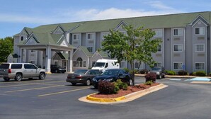 A hotel with a parking lot, multiple cars, and a building with a green roof and white walls.