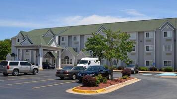 A hotel with a parking lot, multiple cars, and a building with a green roof and white walls.